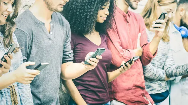 Een rij mensen staat zij aan zij, elk met een smartphone in de hand.