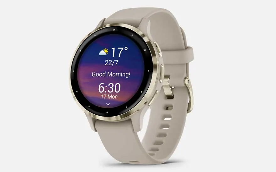 Een beige Garmin Venu smartwatch met ronde wijzerplaat geeft het weer, datum en een ochtendbericht weer.