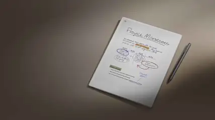 Een wit notitieblok met de titel "Project Mijlpalen" en handgeschreven notities, met een zilveren pen aan de rechterkant, op een bruine achtergrond.