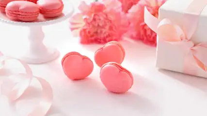 Roze macarons, bloemen, een cadeau en een lint op een witte achtergrond. Macarons op een taartplateau.