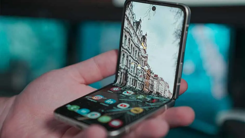 Een hand houdt een opvouwbare smartphone vast, waarop een foto van een gebouw en app-iconen te zien zijn, met een blauwe achtergrond.