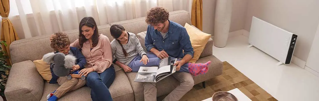 Een gezin van vier geniet op de bank met boeken en plezier. De kamer is warm dankzij een elektrische verwarming op de achtergrond.