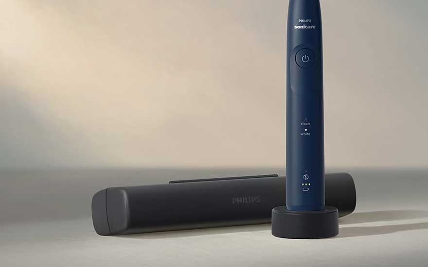 Een blauwe Philips Sonicare staat rechtop op zijn lader, met een gesloten reisetui ernaast in zacht, warm licht.