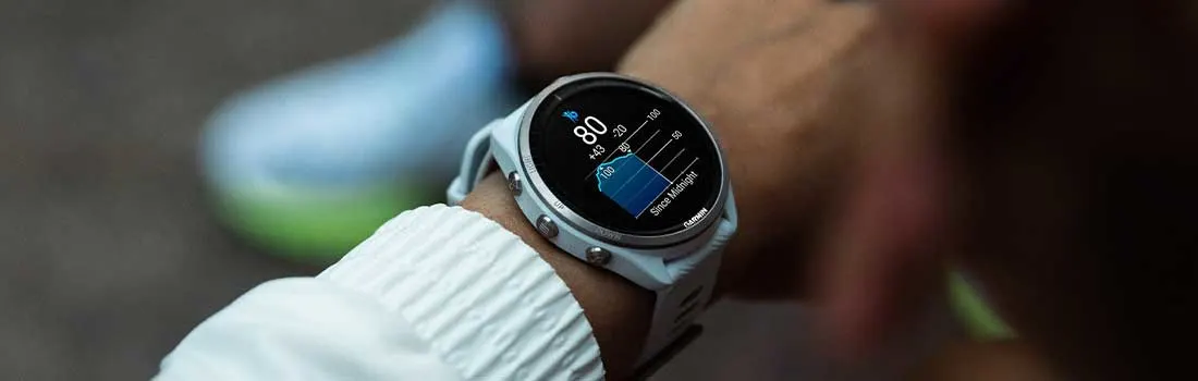 Een sporter controleert zijn slaapgegevens op een Garmin smartwatch tijdens het dragen van een witte sportjas.