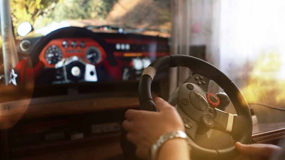 Een persoon speelt een racegame met een stuurwiel voor een scherm dat een auto-dashboard en een racebaan toont.