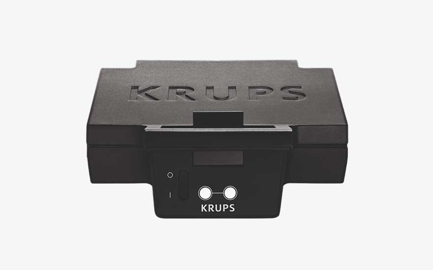 Een compacte zwarte KRUPS-plaat staat frontaal in beeld, met schakelaar en indicatoren op een strakke witte achtergrond.