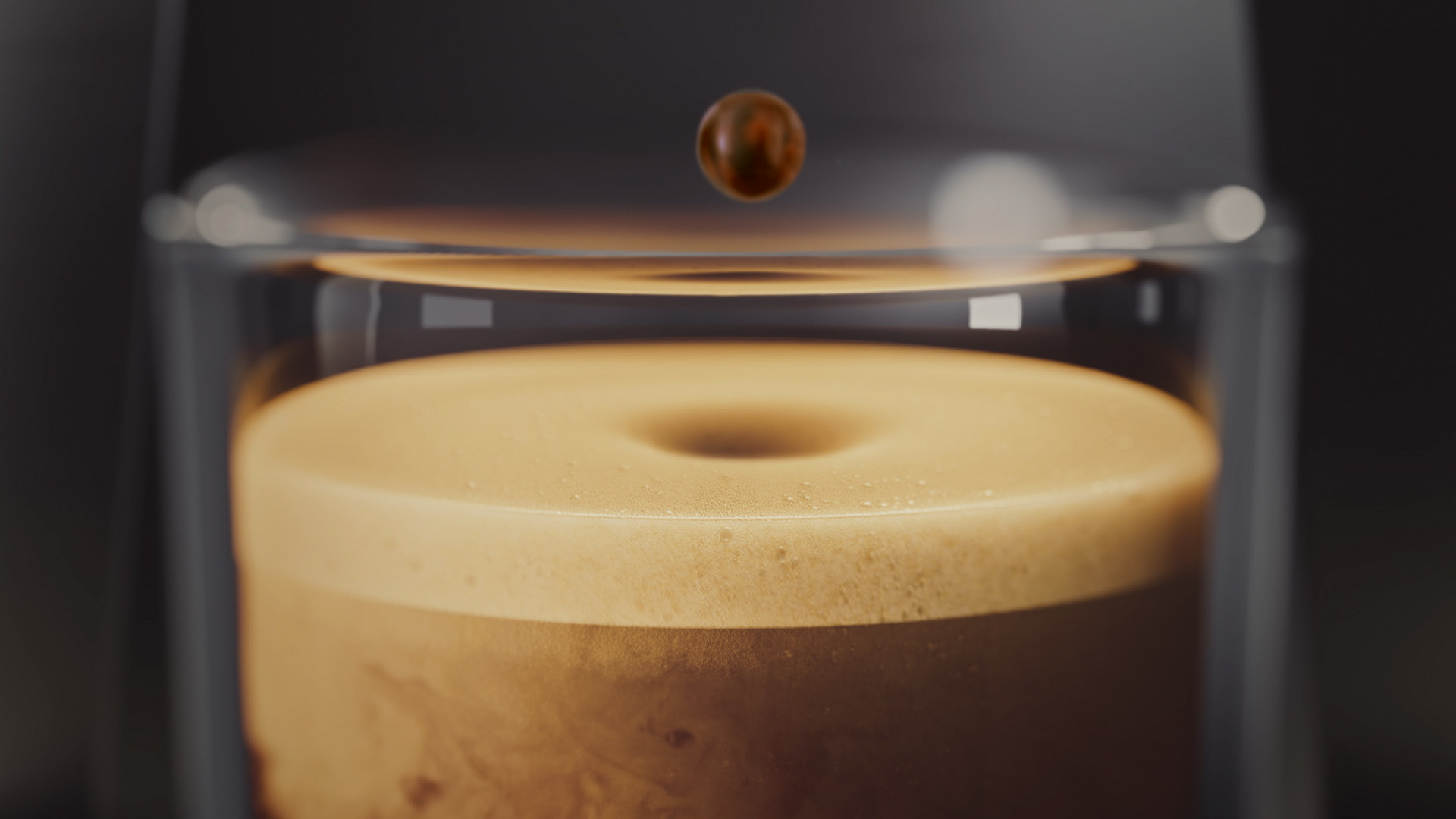 Een heldere glazen beker gevuld met schuimend koffie, met een enkele druppel in de lucht erboven, tegen een donkere achtergrond.