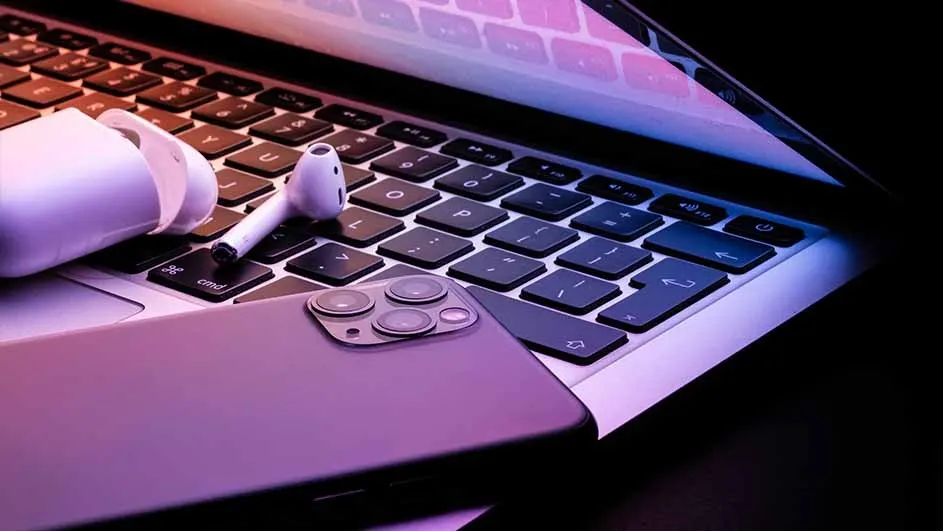 Open laptop with black keyboard, a purple phone and white wireless earbuds are on it.