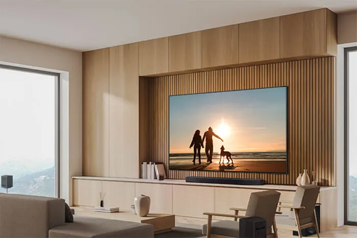 Woonkamer met houten lambrisering, grote ramen, en een tv met een strandscène van mensen en een hond bij zonsondergang.