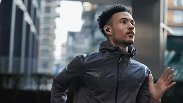 Een persoon rent buiten in een stad met een donkere sportjas en draagt draadloze oordopjes van het merk Sony in zijn oren.