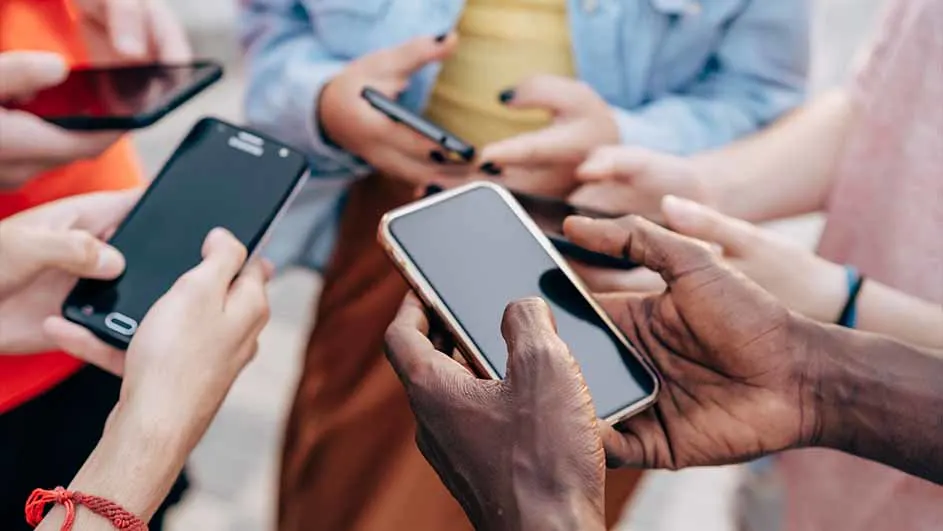 Een groep mensen houdt mobiele telefoons vast. Verschillende telefoons en handen zijn zichtbaar in de foto.
