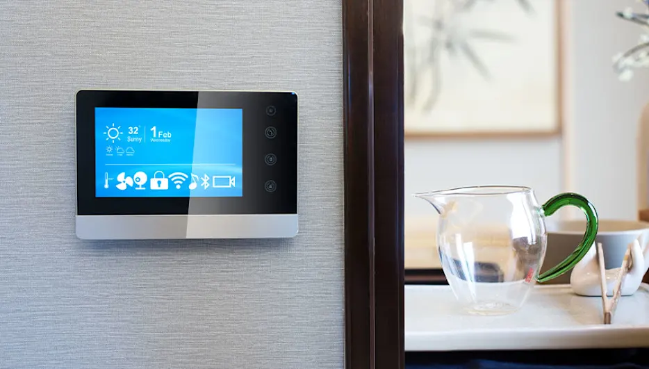 Een smart home bedieningspaneel aan de muur, met een blauw scherm dat de datum, tijd en temperatuur weergeeft.