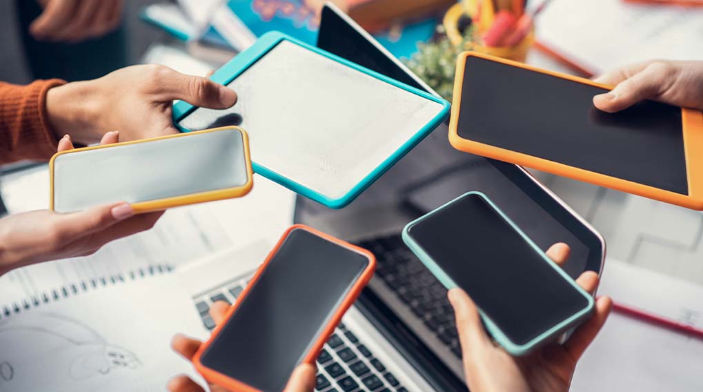 Mensen houden telefoons en tablets vast met gekleurde randen boven een laptop en notitieboekjes.