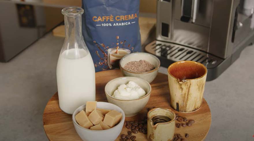 Een houten plank met een fles melk, koffiezak, mokken, koffiebonen en kommen gevuld met room, karamel en chocoladepoeder.