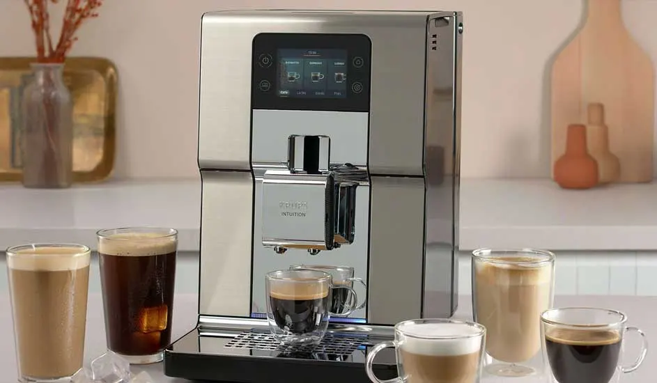 Een zilveren koffiemachine met touchscreen staat op het aanrecht, omringd door zes glazen met verschillende soorten koffie en melkschuim.