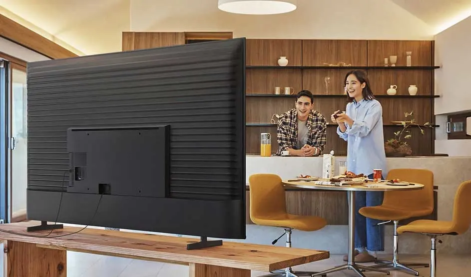 Een groot televisietoestel staat op de voorgrond, terwijl twee mensen samen in een moderne eetkamer staan.