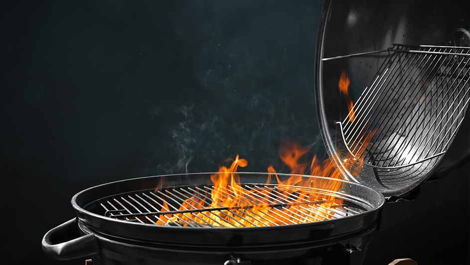 Een zwarte barbecue met vlammen en rook tegen een donkere achtergrond, de deksel staat open.