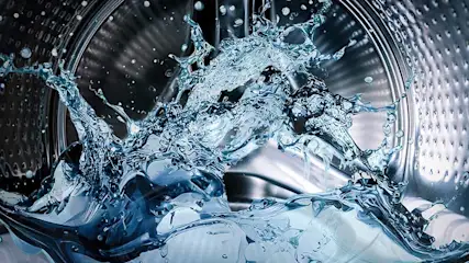 Water spettert in een zilverkleurige wasmachine, met een trommel vol kleine gaatjes en witte was.