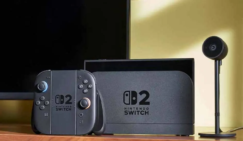 Een Nintendo Switch 2 spelcomputer met docking station en controllers staat op een houten tafel naast een zwarte camera in een moderne woonkamer.