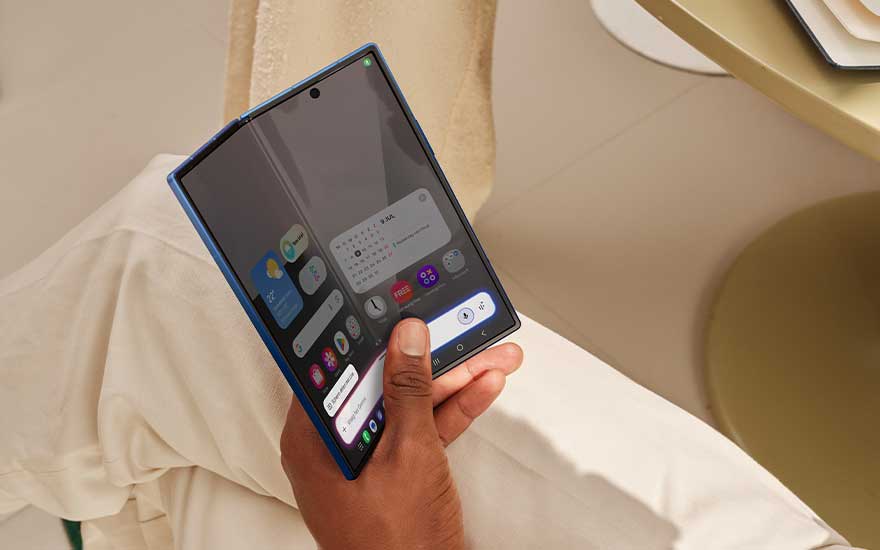 A person uses an unfolded blue smartphone like a small tablet, with widgets and notifications visible on the wide screen.