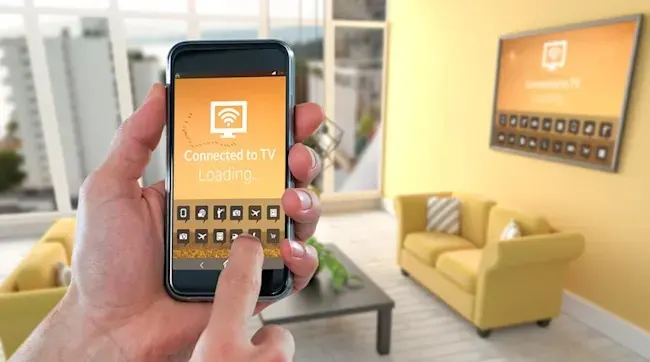 Hand houdt een telefoon vast met een scherm 'Verbonden met TV'. Gele bank en tv aan een gele muur.