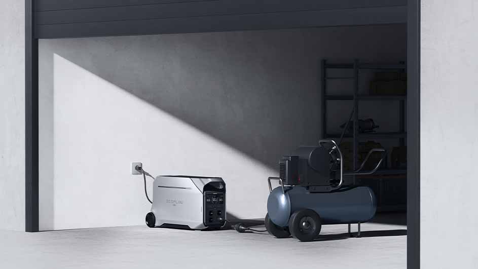 In een garage staan een grijze generator aangesloten op een stopcontact, en een blauwe compressor met wielen.