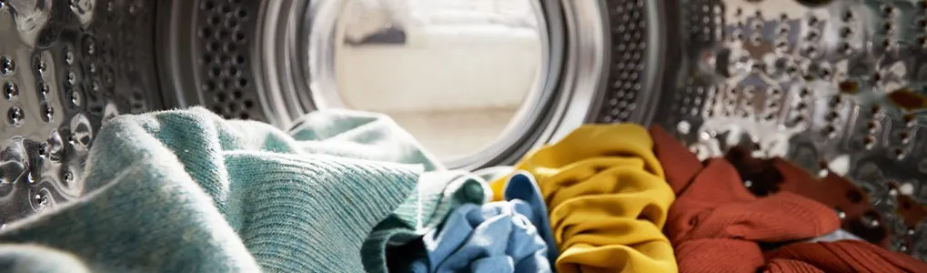 Inside a washing machine drum, multiple colored clothes are visible through the porthole.