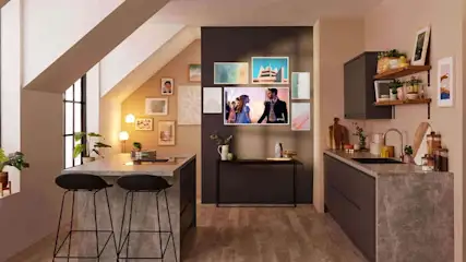 A modern kitchen setting with a TV mounted on the wall among several artworks, complemented by an island with two stools.