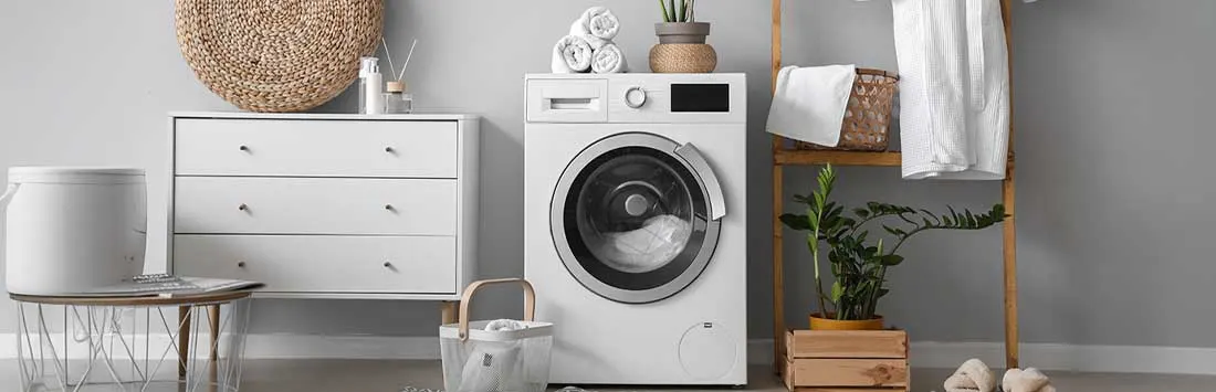 Een nette wasruimte toont een witte wasmachine, ladekast, planten en handdoeken; alles oogt licht, rustig en verzorgd.