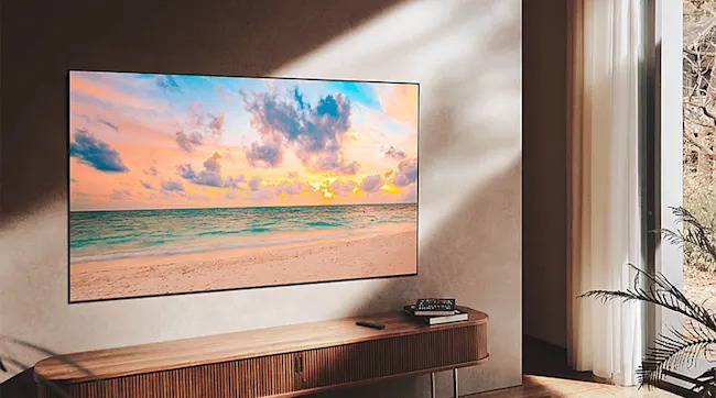 Een moderne woonkamer met een grote tv aan de muur die een kleurrijk strand laat zien, naast een houten meubel en een raam met gordijnen.