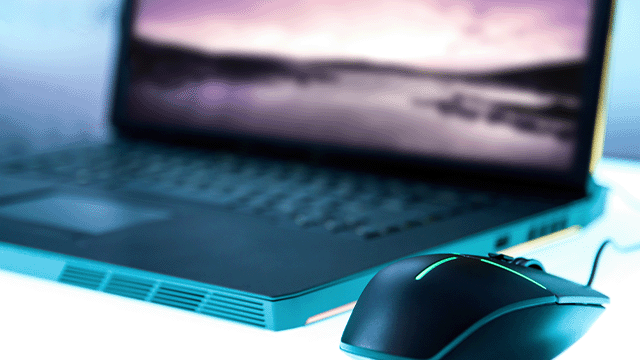 Een laptop staat open met een scherm dat een landschap toont, naast een zwarte muis met een kabel.