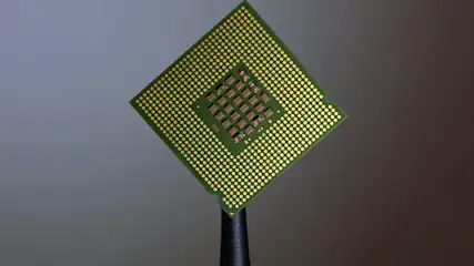 Groene vierkante computerprocessor met gouden pinnen staat op een zwarte standaard tegen een grijze achtergrond.