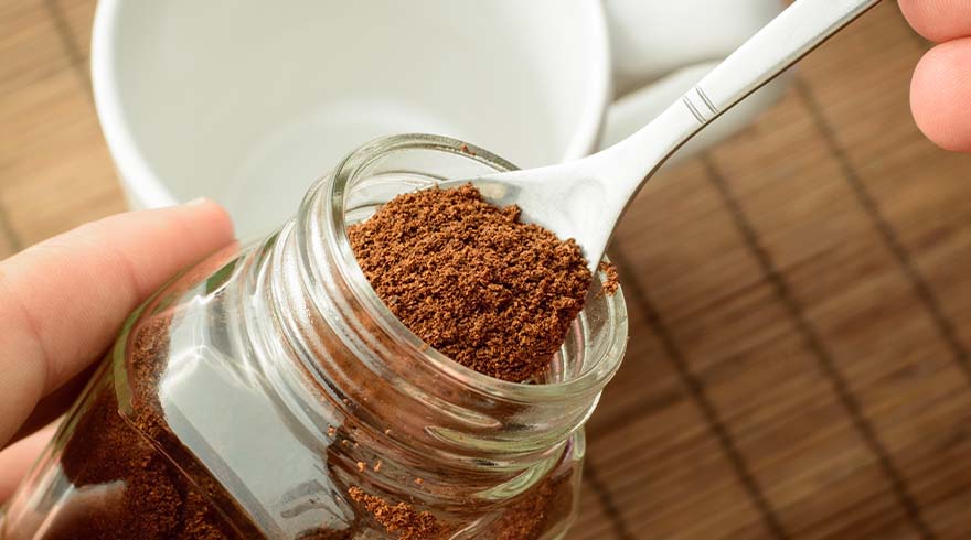 Een glazen pot met bruin poeder, een lepel en een witte mok op een houten tafel.