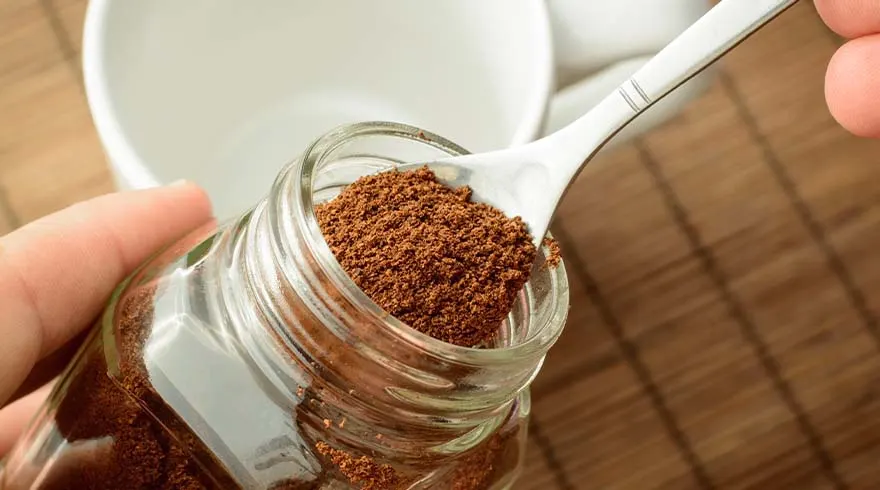 Een glazen pot met bruin poeder, een lepel en een witte mok op een houten tafel.