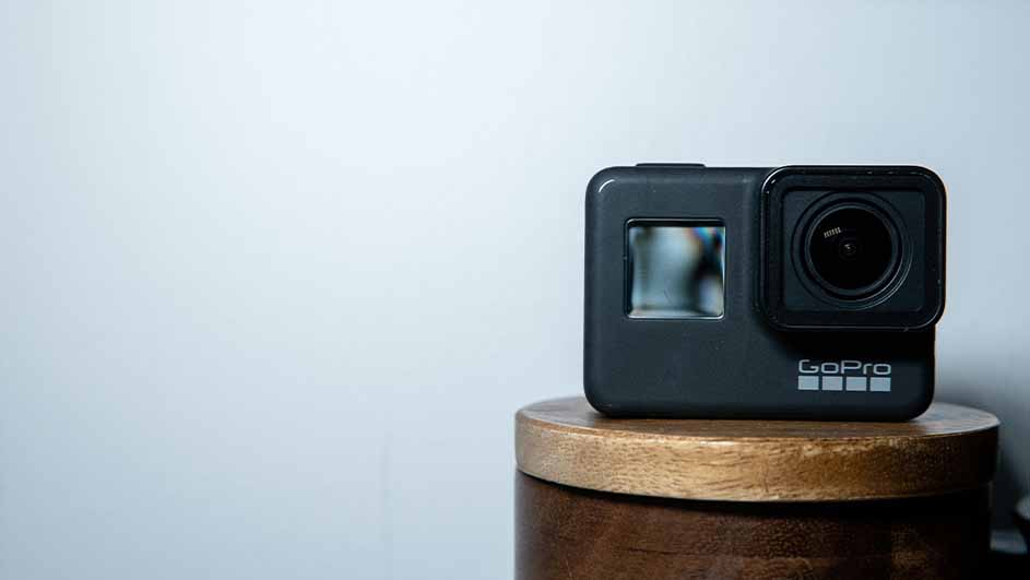 Een zwarte GoPro-camera staat op een bruin houten oppervlak tegen een lichtblauwe achtergrond.