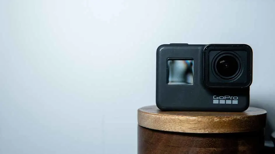 Een zwarte GoPro-camera staat op een bruin houten oppervlak tegen een lichtblauwe achtergrond.