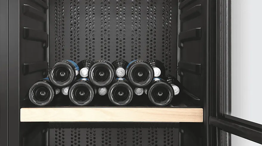 Wijnflessen liggen op een houten plank in een zwarte wijnkoelkast met gatenpatroon.