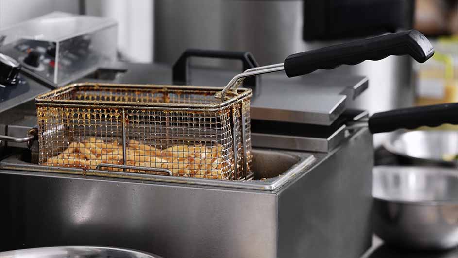 Friteuse met een metalen mand vol friet. De mand hangt boven een metalen bak. Zwarte handvatten aan de zijkant.