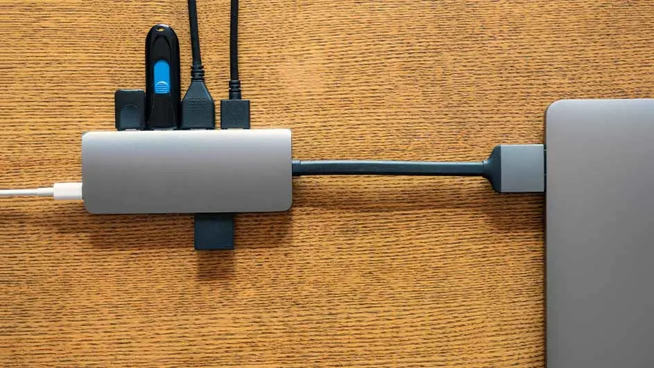 Een grijze USB-hub is aangesloten op een grijze laptop op een houten oppervlak met verschillende stekkers erin.