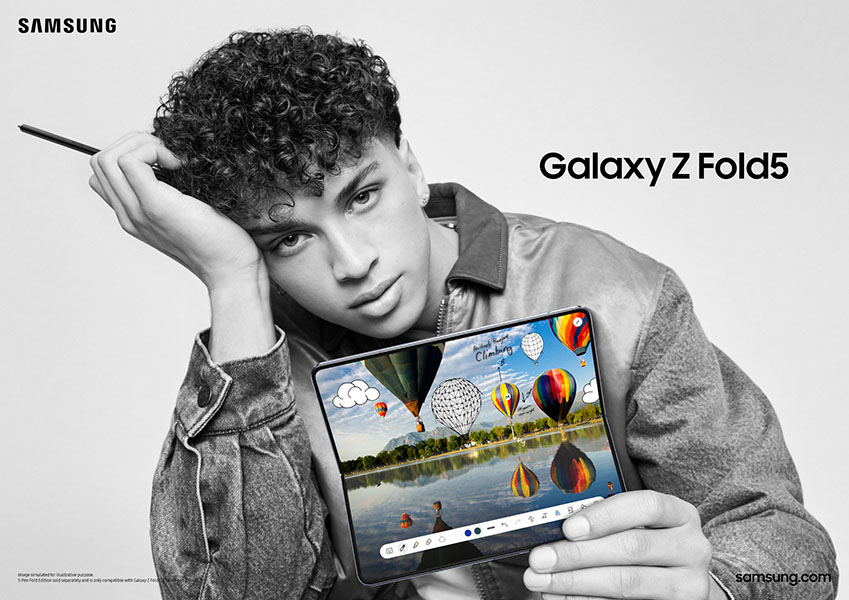 Een persoon houdt een Samsung Galaxy Z Fold5 vast met een scherm waarop luchtballonnen boven een meer te zien zijn. De achtergrond is effen.
