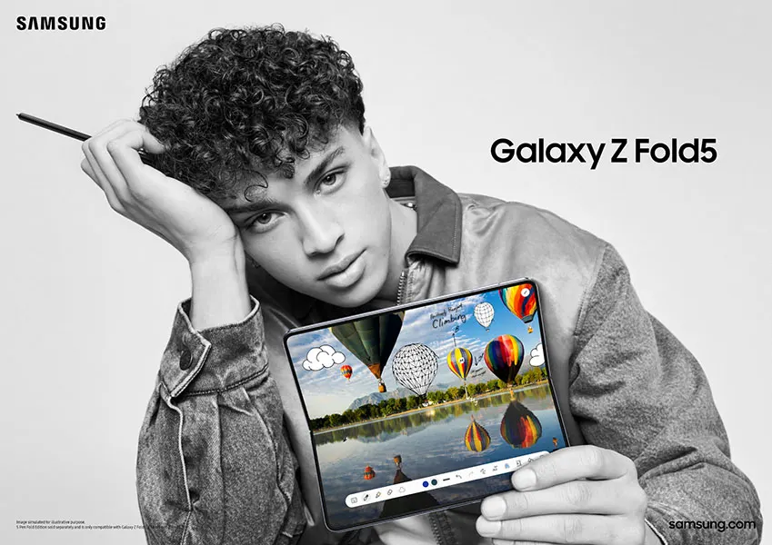 Een persoon houdt een Samsung Galaxy Z Fold5 vast met een scherm waarop luchtballonnen boven een meer te zien zijn. De achtergrond is effen.