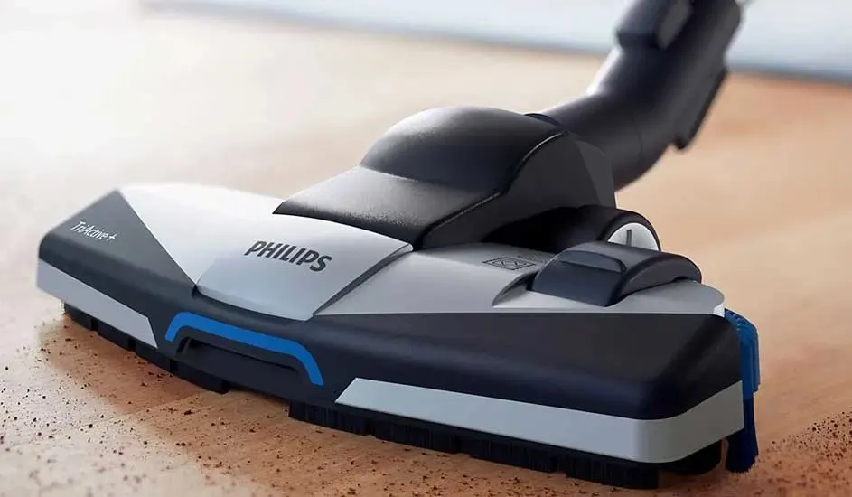 Close-up of a Philips TriActive vacuum head gliding over a wooden floor, with blue accents and soft bristles capturing fine dust.