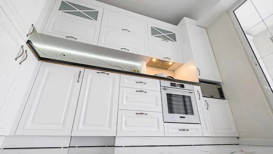 Een keuken met witte kasten, zilveren handgrepen en een oven. Er is ook een zilveren magnetron en een licht onder de bovenkasten.