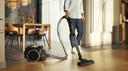 Een persoon stofzuigt een houten vloer met een klassieke sledestofzuiger, ideaal voor dagelijks schoonmaken.