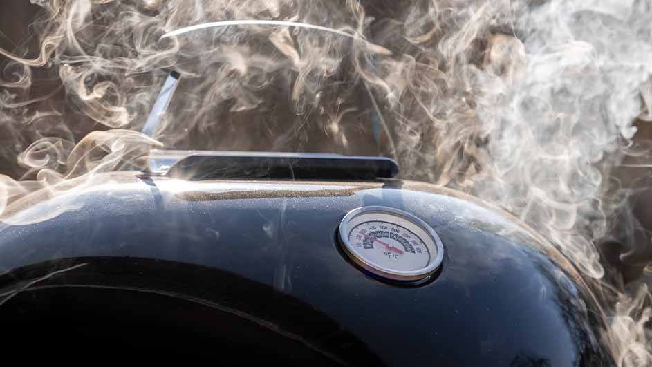 Een zwarte barbecue met een thermometer en opstijgende rook.