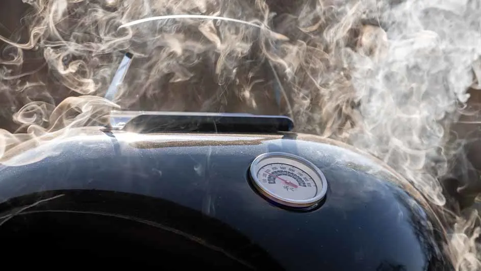 Een zwarte barbecue met een thermometer en opstijgende rook.