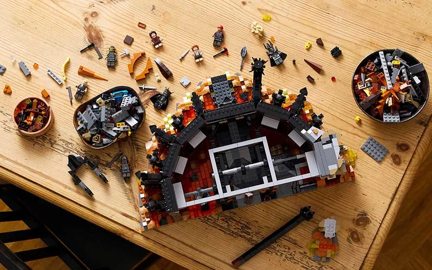 Bovenaanzicht van een grote LEGO-bouwset op een houten tafel, met losse stenen, minifiguren en kommetjes vol onderdelen.