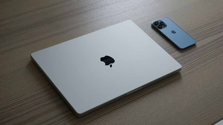 A silver laptop with a black logo sits on a wood grain surface next to a blue smartphone.