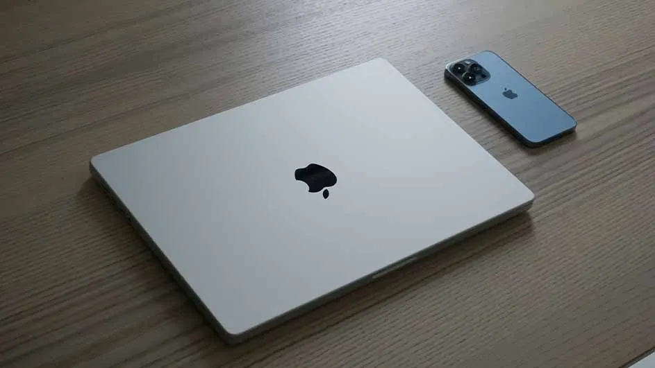 A silver laptop with a black logo sits on a wood grain surface next to a blue smartphone.