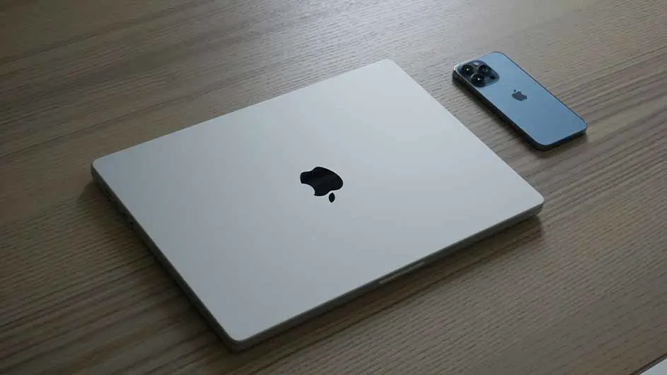 Een gesloten MacBook en een iPhone liggen naast elkaar op een houten tafel, beide met het Apple-logo zichtbaar.